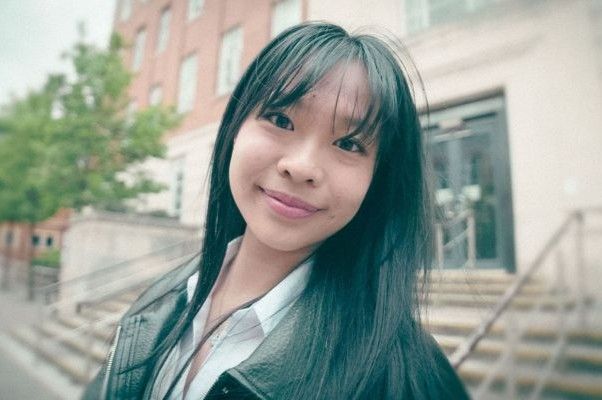 A student smiles back at the camera. They are on campus.