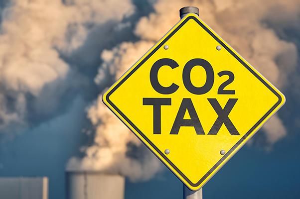 A sign saying CO2 tax in front of a power plant releasing vapour into the atmosphere.