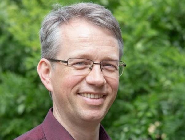 Headshot of person with glasses in front of greenery