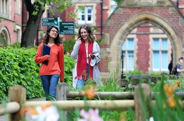 Two students walking down a path in front of the Great Hall. There are some flowers in the foreground.