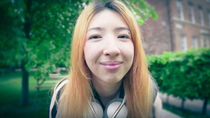 A close up of a student smiling at the camera. They have headphones around their neck.