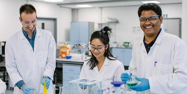 Three researchers in a lab wearing lab coats and holding test tubes and beakers.