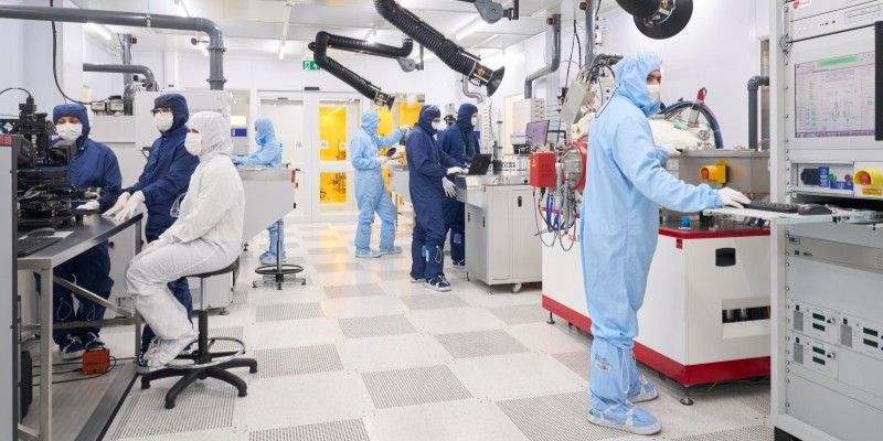  Eight users wearing protective body suits, hoods and overshoes, interacting with various instruments within a well-lit processing bay.