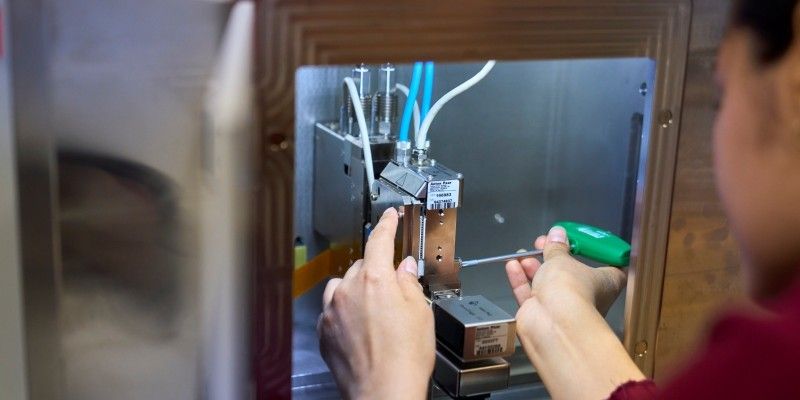  A technician's hands adjust a metal sample loading component using a metal tool with a green handle. 