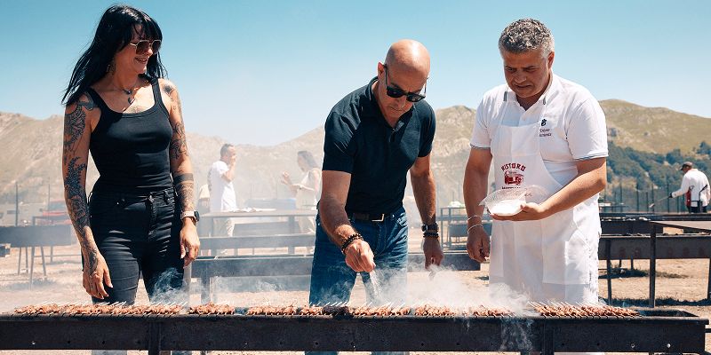 Stanley Tucci cooks alongside a man and a woman at an outdoor barbecue