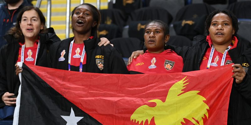 Joanna stands with four PNG players behind a PNG flag singing the national anthem
