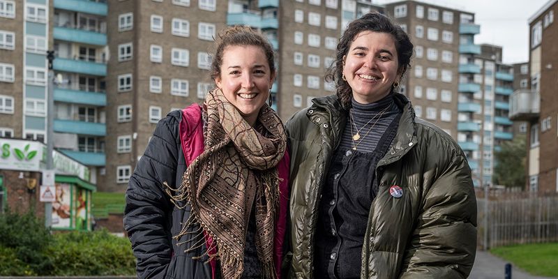 Keziah and Tamsin stand in front of a block of flats