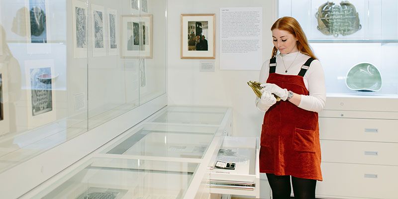 Student wearing gloves examines an object in Treasures Gallery
