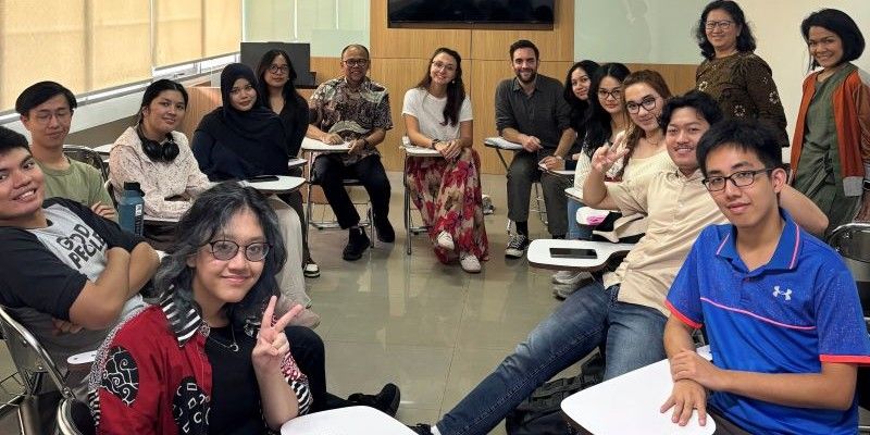 A diverse group of people sitting on chairs in a circle all smile at the camera.