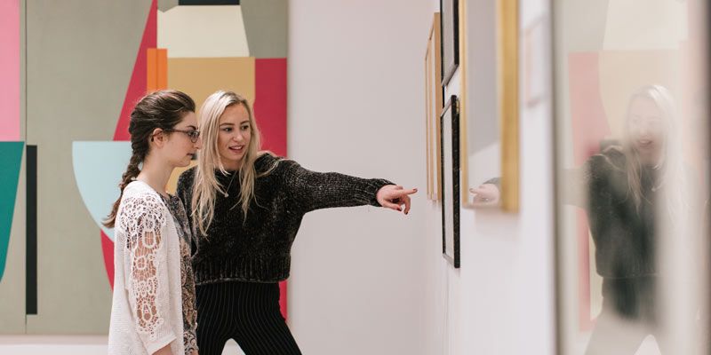 Two students looking at art on a gallery wall and chatting about it