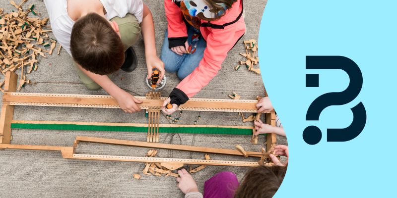 A group of children taking apart a wooden mechanism from inside a piano. Two children are using screwdrivers. Also the logo for Be Curious, which is a question mark and a letter B combined.