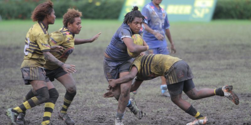 A rugby player tackles the ball carrier on a muddy field in PNG
