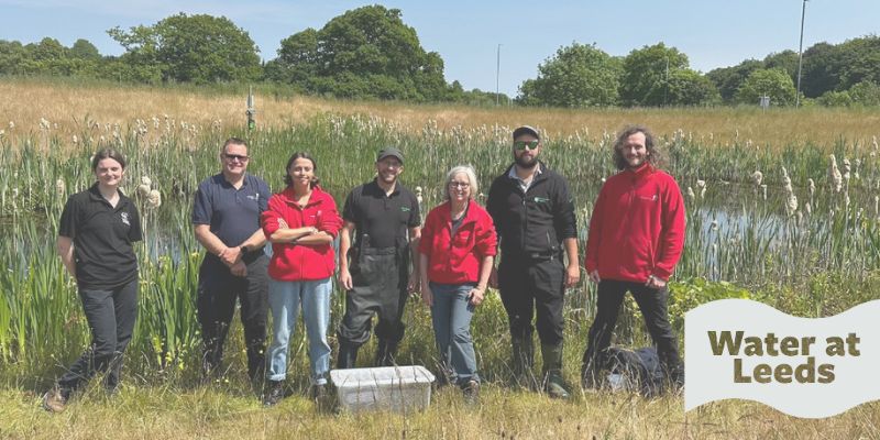 A group of biology researchers at a beck, all smiling at the camera. The wave-shaped logo in the corner reads Water at Leeds.