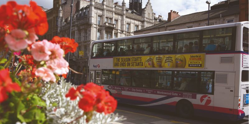 Bus driving through Leeds city centre on a sunny day with flowers in the foreground