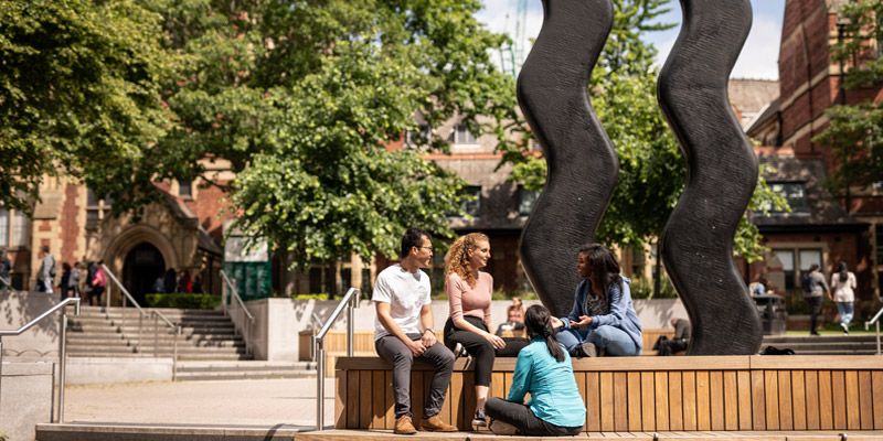 A group of students chat next to a sculpture on campus. January 2020