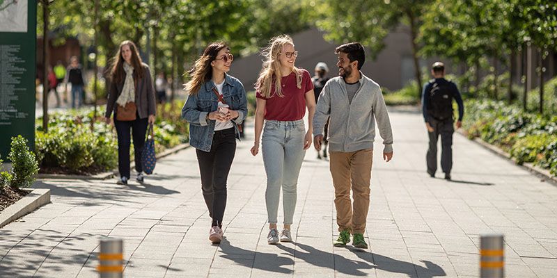 Three students walking through campus on a sunny day. They are smiling.