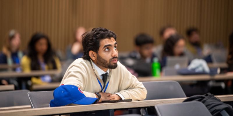 Farhan leaning on a table he is sat at, focusing intently on a presentation