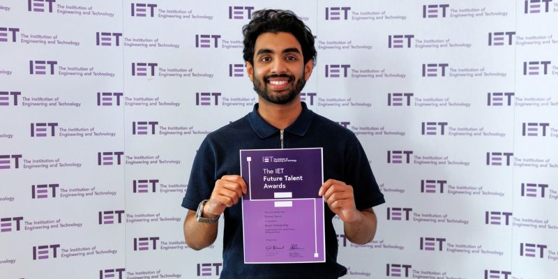 Farhan stands in front of a white background holding his IET Future Scholarship award