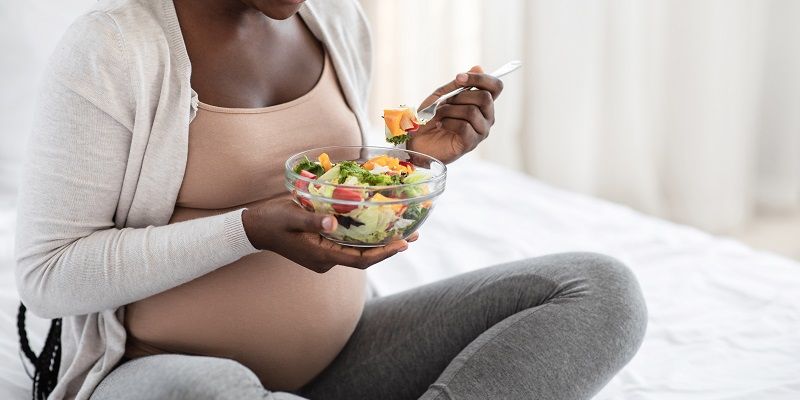 A pregnant woman eating a salad on a bed