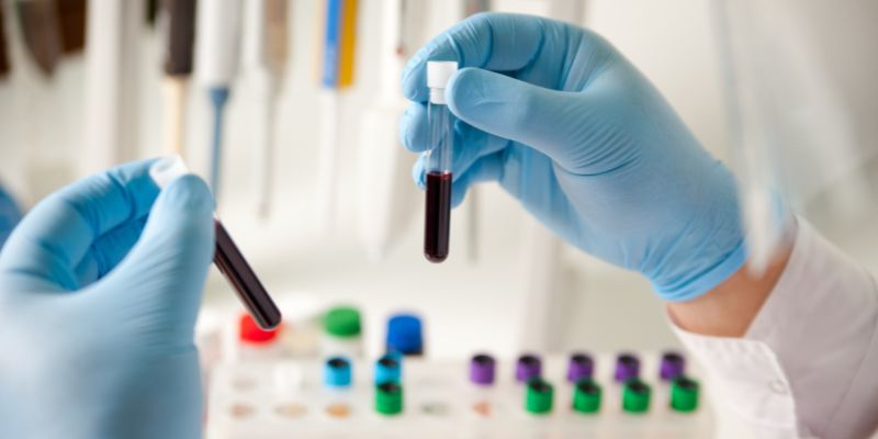 A pair of hands in blue gloves holding blood samples in a lab