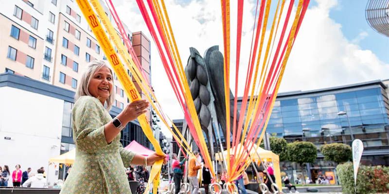 A smiling person stretching ribbons across an open space.