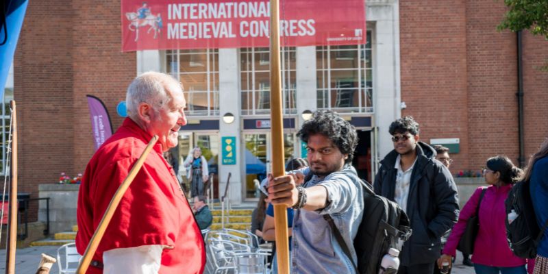 A person holds a bow and arrow at the International Medieval Congress, instructed by a specialist.