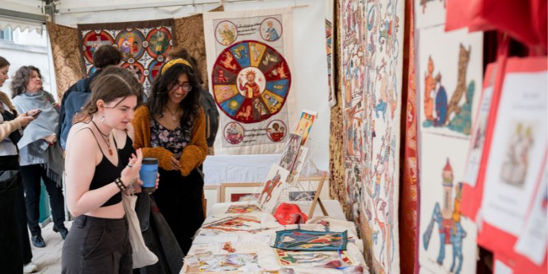 Two people look at tapestries at the International Medieval Congress craft fair.
