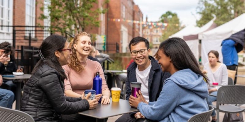 Four international students sitting at a table outside Leeds University Union building, with hot drinks.