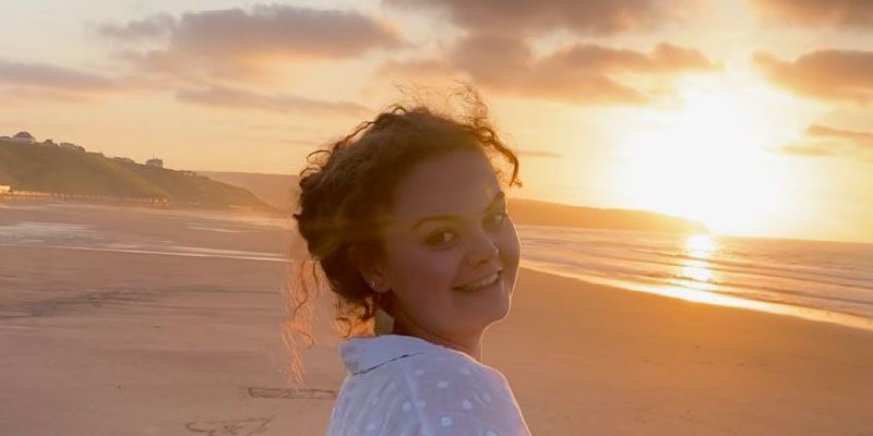 A student on the beach at sunset, looking over their shoulder and smiling