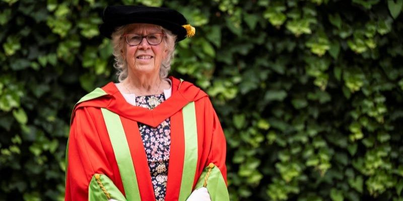 Judith Blake stands in red and green graduation gowns.