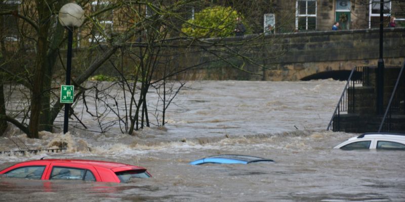 Three cars submerged in water as a street floods. Behind is a bridge, its arch nearly completely submerged in water.