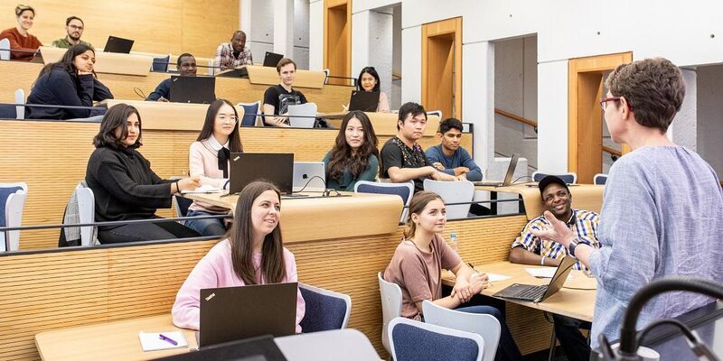 A lecture theatre with a lecturer at the front and students sitting in rows with laptops in front of them.