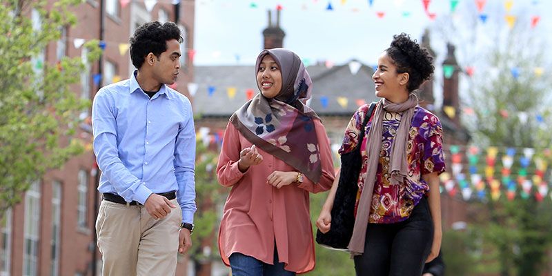 Three students walking together outside Leeds University Union while in conversation.