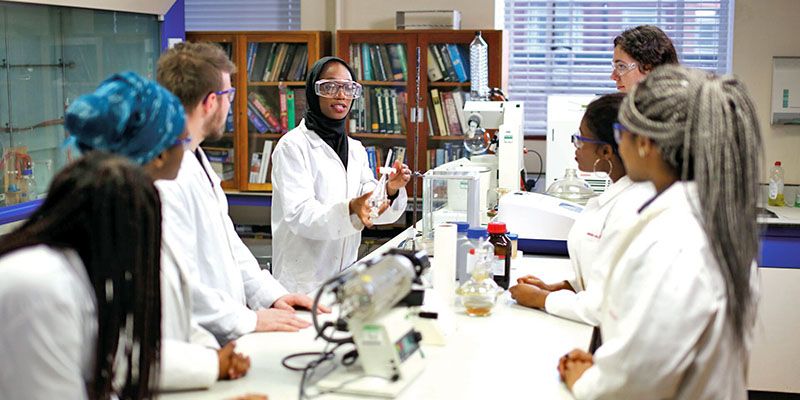 Postgraduate researchers in lab coats stood around laboratory equipment.