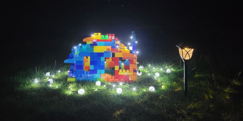 Colorful block structure lit by string lights on grass at night, with a small garden lamp nearby."