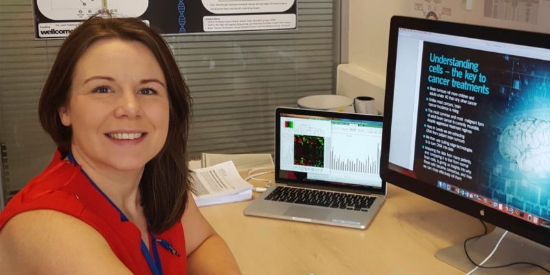 Dr Lucy Stead smiles as she sits at her desk which has a laptop and monitor screen on it