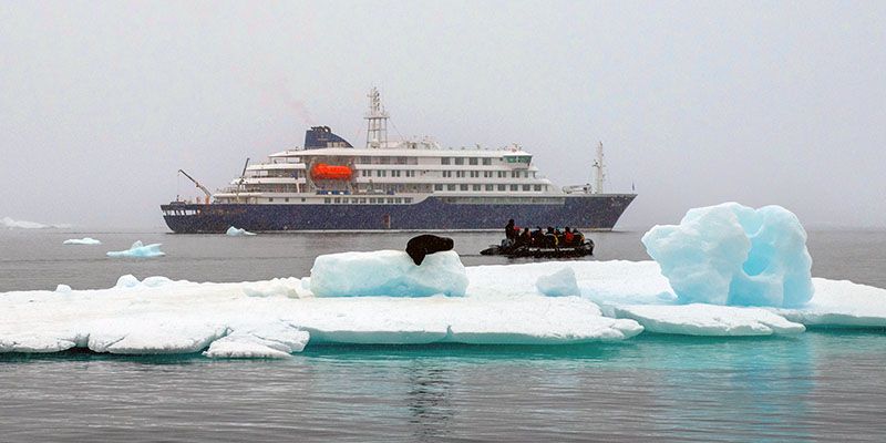 MV Hondius behind a small boat and an iceberg.