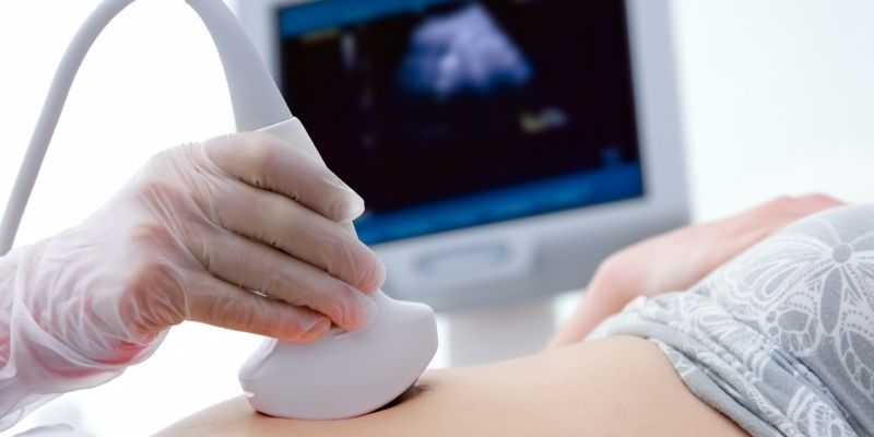 A sonographer carrying out an ultrasound on a stomach with a monitor in the background