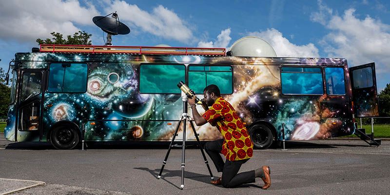 A highly decorated bus featuring space and planets, with a person operating a telescope in the foreground.