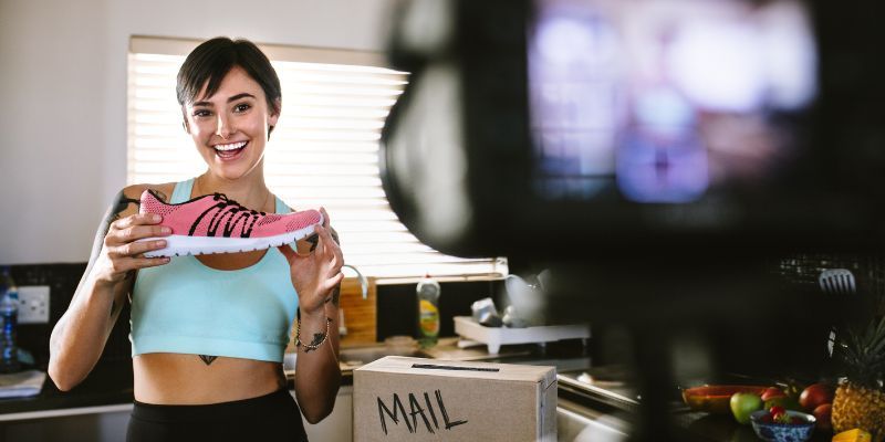 An influencer holds a pink shoe in front of a camera.