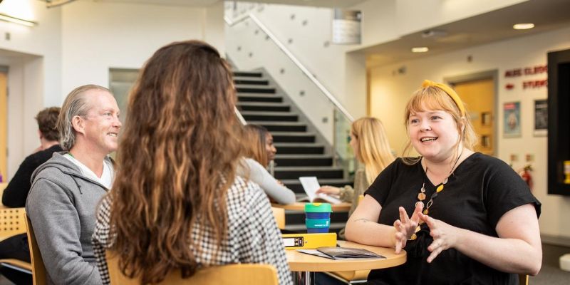 Three postgraduate researchers at table in foyer of The Stage building on campus