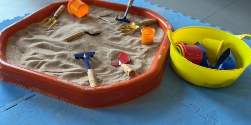 A children's sandpit with toys, buckets and spades
