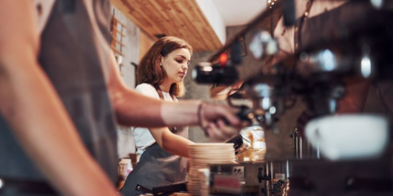 A young woman working as a barista makes coffee.