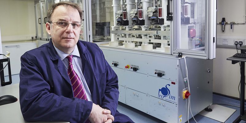 Professor Richard Hall from the School of Mechanical Engineering at the University of Leeds, sitting in his lab, in front of a machine that physically tests artificial joints.