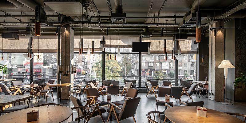 Tables in an empty restaurant with ventilation ducts on the ceiling.