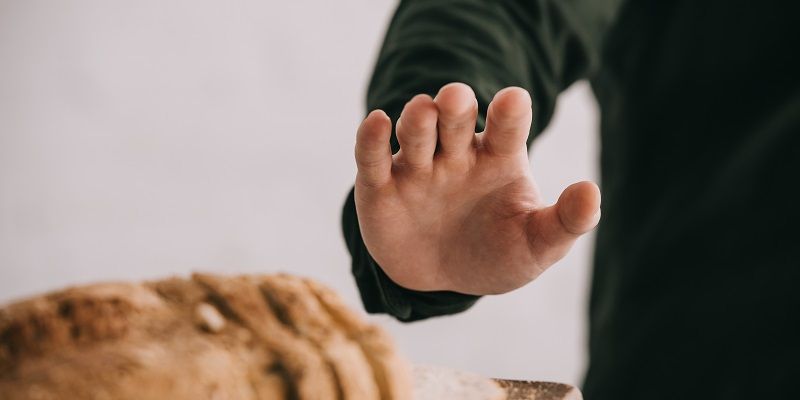A man is holding his hand up above a loaf of bread in a gesture that suggests he is saying no to bread,