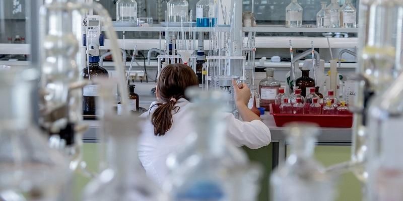 The image shows the back of a scientists standing at a laboratory bench surrounding with chemistry equipment