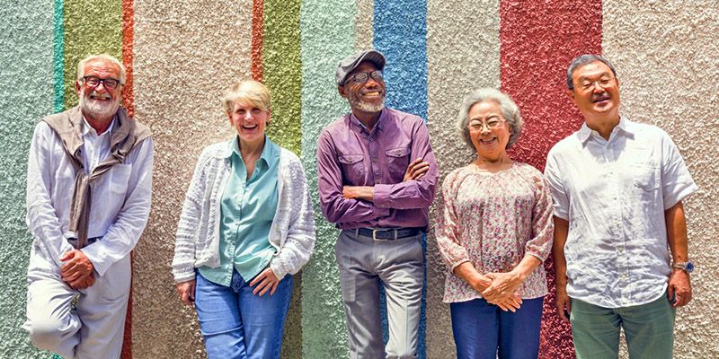 Five senior people stood smiling in a line, before a brightly painted wall.