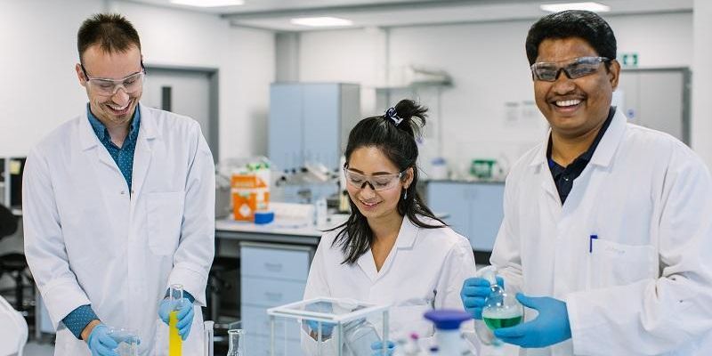 Three researchers in a lab wearing lab coats and holding test tubes and beakers