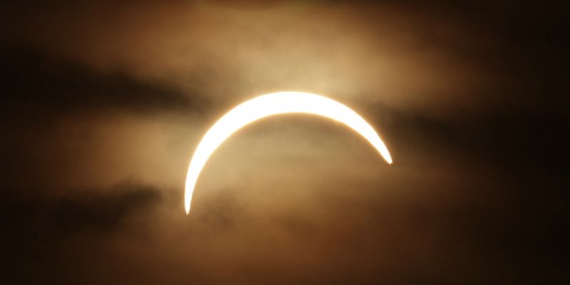 The moon moves in front of a sun in a cloudy sky